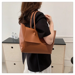 Close-up of brown leather tote bag with flap closure worn by a model in casual setting