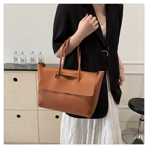 Close-up of a brown leather tote bag with flap closure worn by a model on shoulder