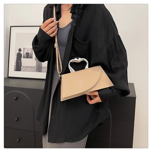 Détail d'un sac bandoulière beige avec poignée argentée sur la tenue noire d'un mannequin