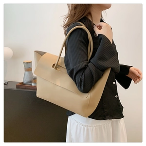 Chic beige leather tote bag with unique flap design styled for shoulder wear on a model
