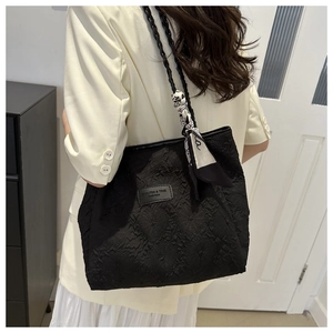 Detail of black textured tote bag with woven drawstring and patterned silk scarf accent