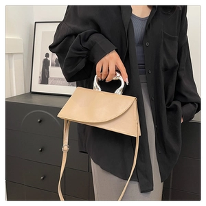 Détail du sac beige en cuir avec poignée anneau argentée et rabat au design asymétrique