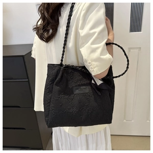 Detail of black textured tote bag with woven strap and silk scarf accent on model