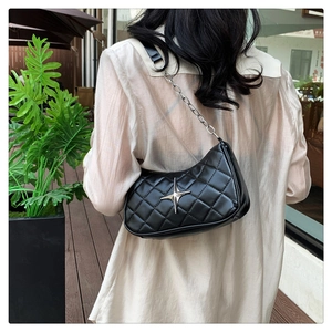 Detail of black quilted shoulder bag with silver star charm worn by a model in a garden