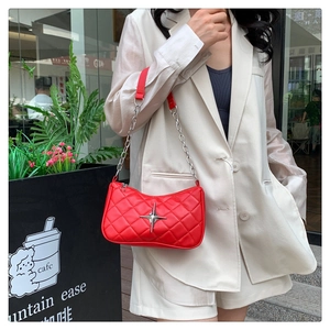 Detail shot of a red quilted shoulder bag with silver star emblem and chain strap