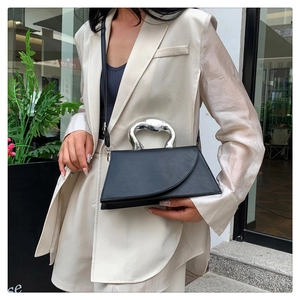 Close-up of asymmetrical black leather handbag featuring unique silver metal handle