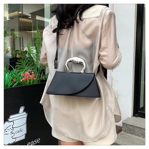 Détail d'un sac à main noir avec poignée argentée incurvée porté par un mannequin