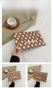 Detail of a brown woven envelope clutch with a V-shaped flap and gold metal bar accent