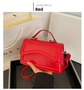 Détail d'un sac à bandoulière en cuir rouge avec rabat ondulé et boucle dorée