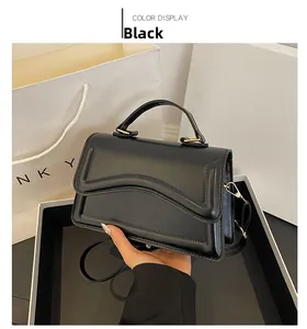 Détail d'un sac noir avec texture ondulée et boucles dorées sur emballage de luxe blanc