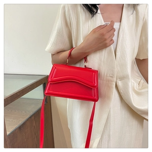 Detail of red crossbody bag with scalloped flap and gold hardware on silk blazer