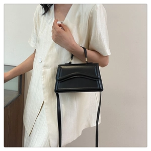 Detail of a black matte textured handbag showing wave flap design and metal hardware