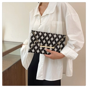 Detail of checkered woven envelope clutch with gold metal bar closure held by model