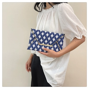 Détail d'une pochette enveloppe tissée bleue et blanche avec boucle en métal doré