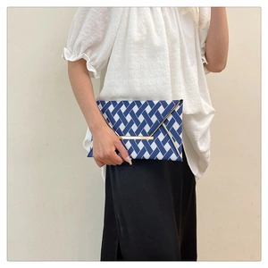 Détail d'une pochette enveloppe tissée bleue et blanche avec garniture métallique en V