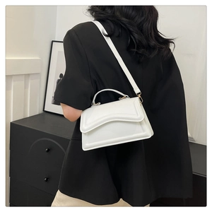 Vue détaillée d'un sac à main blanc en cuir verni porté sur un blazer noir élégant
