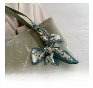 Detailed close-up of light green pleated tote bag with stylish silk scarf handle decor