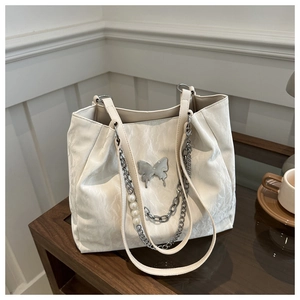 Chic beige tote bag with silver butterfly charm and pearl chain on a wooden table