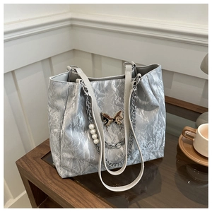 Detail of silver tote bag featuring crushed texture, metal butterfly and pearl chain
