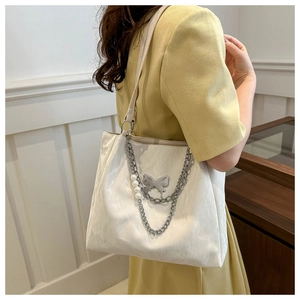 Detail showing white pleated tote bag with large metal butterfly and pearl chain strap