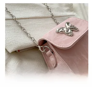Detail of pink mini chain bag featuring glossy patent texture and silver butterfly ornament