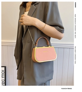 Detail of pink leather box bag with gold metal trim and chain strap on a gray blazer