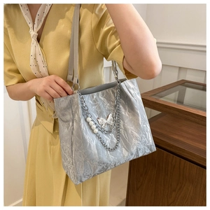 Close-up of silver tote bag with metallic texture, pearl charms and metal chain details