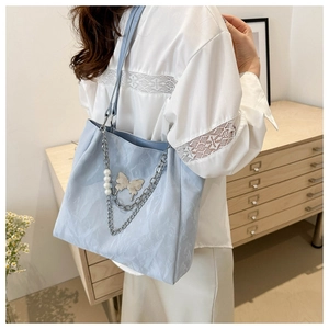Detail of light blue tote bag featuring silver butterfly charm and pearl chain accent