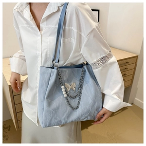 Detail of light blue tote bag featuring cloud pleats and silver butterfly with pearl chain