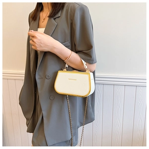 Close-up of a white box clutch with gold metal trim and chain strap carried by a model