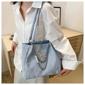 Detail of light blue tote bag featuring silver butterfly buckle and pearl chain