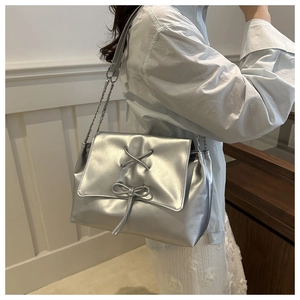 Detail of silver metallic shoulder bag with decorative crisscross lacing and bow