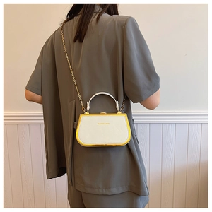 Close-up of white crossbody bag with gold metal frame and slim chain strap on model