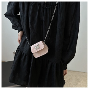 Detail of pink mini crossbody bag with silver butterfly charm and metal chain on black dress