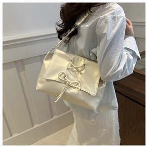 Detail of pearlescent beige tote bag featuring decorative lace-up bow and chain strap