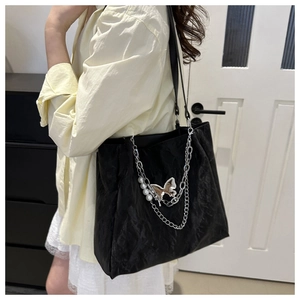 Detail of black pleated tote bag featuring silver chain with pearl and butterfly charms
