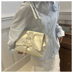 Detail of champagne satin shoulder bag featuring elegant bow tie and chain strap design