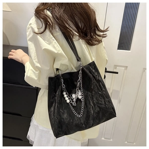 Detail of black pleated tote bag featuring silver chain, pearls, and butterfly pendant