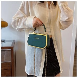 Detailed shot of dark green box bag with gold metal trim and chain strap held by hand