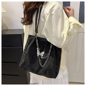 Detail of black pleated tote bag featuring silver chain and butterfly pearl pendant charm