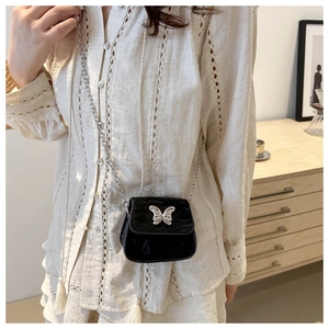 Mini black velvet crossbody bag with silver butterfly buckle and chain strap on a white shirt