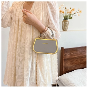 Detail of grey mini box bag with gold metal frame and fashion text on white lace dress