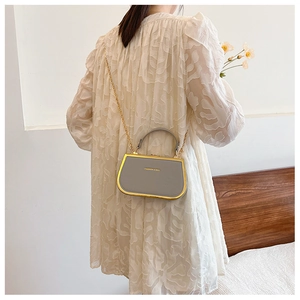 Gray leather crossbody bag with gold chain strap shown on model in a modern room