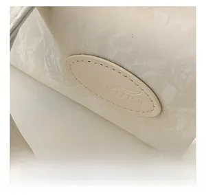 Detail of cream marbled leather texture with embossed oval patch and precise stitching
