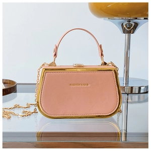 Detail view of pink box handbag with gold frame and chain strap on a glass table