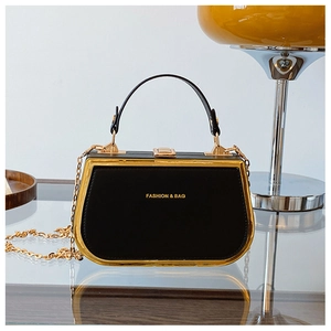 Close-up of black box handbag with gold frame and chain strap on reflective surface