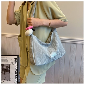 Detail of silver pleated shoulder bag with cute plush dog pendant and smooth metallic texture