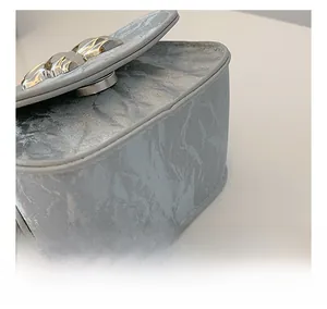 Détail du sac plissé argenté montrant des coutures doubles et un fermoir rond en métal