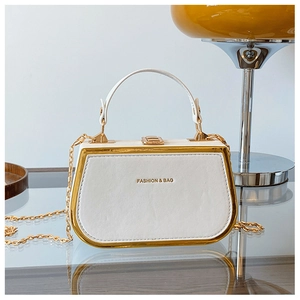 Detail of white leather box bag with gold metal trim and chain strap on glass table
