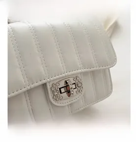 Close-up of white vertical quilted handbag featuring a crystal-embellished turn-lock closure